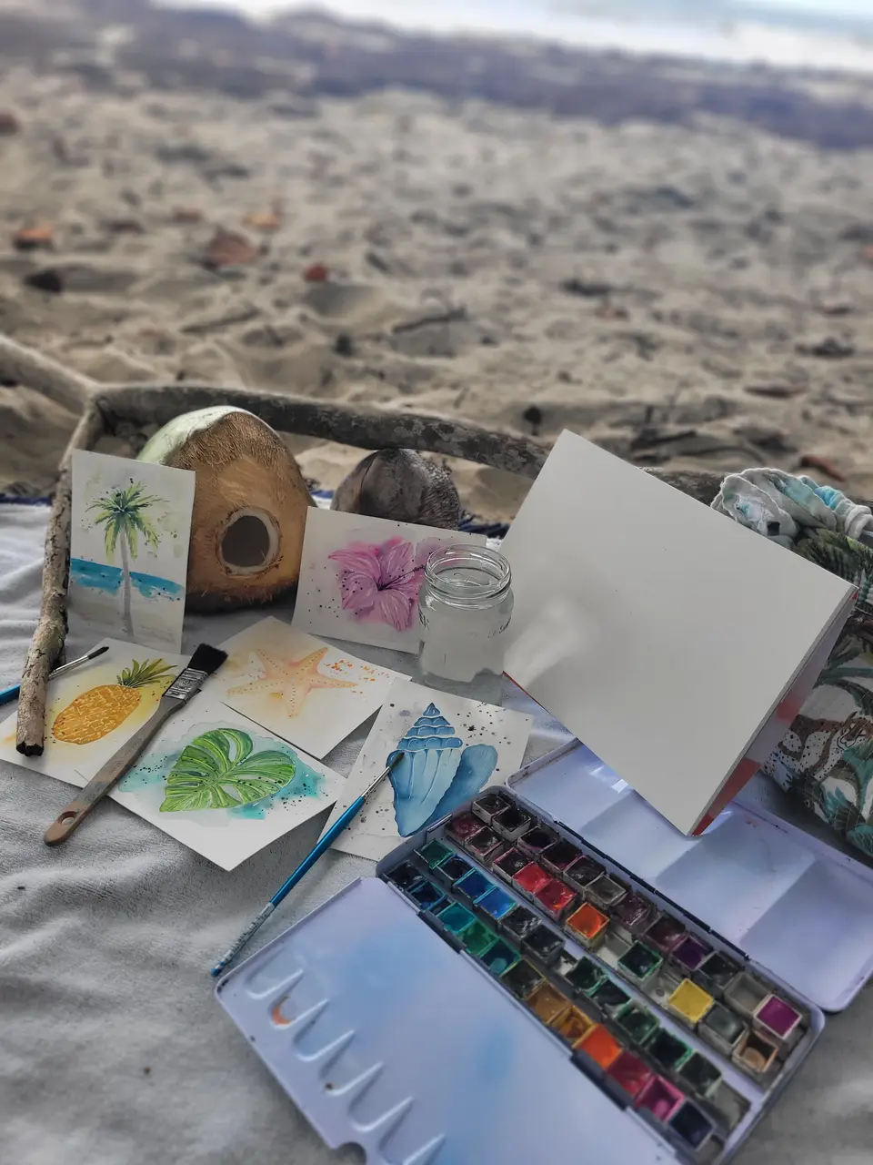 Matériel d’aquarelle installé sur le sable de la plage du Diamant : palette, pinceaux et cartes